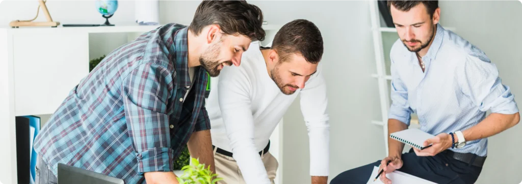 Three men are working together at a table.